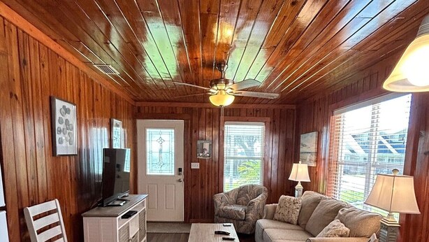 L’intérieur d’un chalet accueillant, avec des murs en bois, un plafond en bois, une table à manger, un canapé, une chaise, un petit meuble blanc et un téléviseur.