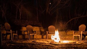 A campfire with plastic chairs arranged around it, set against a stone wall in a wooded area. - #2Cabins cottages,fishing,creeks, ponds,nature trails,anniversaries celebrations (Oneida)