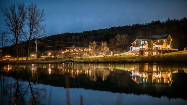 Une propriété au bord du lac, avec une grande maison dotée d’une terrasse et de panneaux solaires, entourée d’arbres et comprenant un quai.