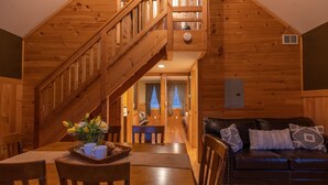L’intérieur d’un chalet en bois comprend un coin repas, un escalier et un salon avec un canapé en cuir.