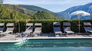 A pool area with lounge chairs and an umbrella, surrounded by lush greenery and mountains in the background. - Villa Eufemia - Country farmhouse with pool (Piano)