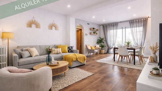 En rummelig opholdsstue med sofa, sofabord og spisebord, med et moderne design og naturligt lys fra store vinduer.