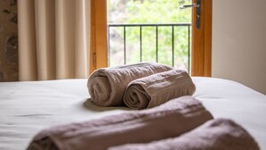 A bed with two rolled towels and a view of greenery through an open door. - La Mazette, les pieds dans l'eau (Olargues)