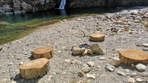 A natural setting with a clear water body, rocky terrain, and wooden stools. - La Mazette, les pieds dans l'eau (Olargues)