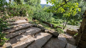 Stone steps leading to a garden with a stone wall, greenery, and a view of a mountain. - La Mazette, les pieds dans l'eau (Olargues)