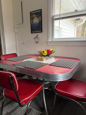 Un comedor con una mesa y sillas rojas, un frutero y un cuadro en la pared.