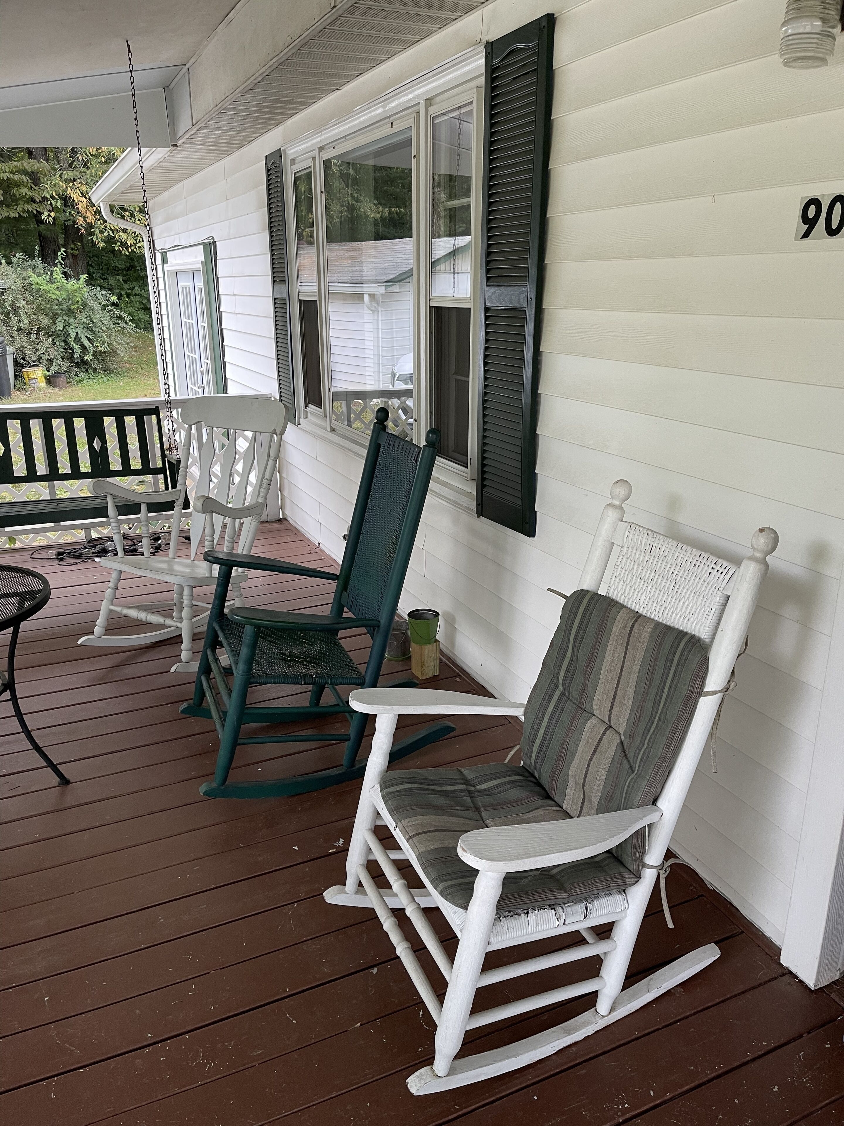 Een veranda met witte schommelstoelen en een tafel, een houten terras en huisnummer 90.