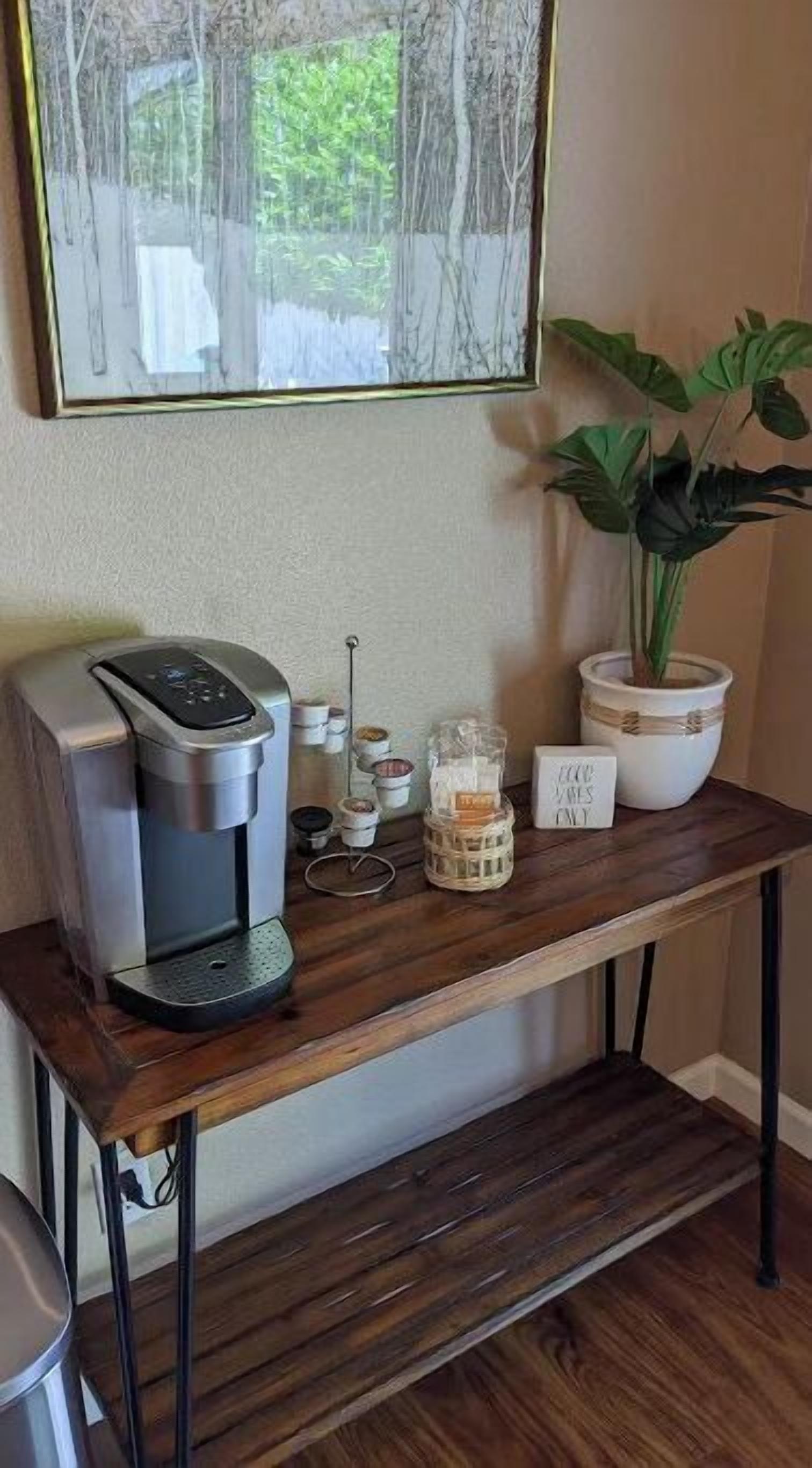 Eine hölzerne Kaffeestation mit Kaffeemaschine, Gläsern und einem Topfpflanzen.