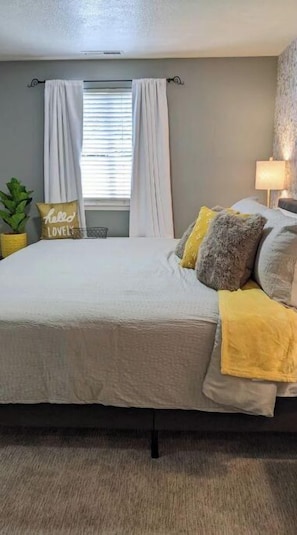A neatly made bed with a white duvet, a bedside lamp, and a window with white curtains.