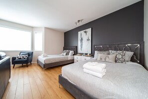 Two single beds with matching headboards and a dark armchair sit beneath a large window and a contemporary abstract painting.