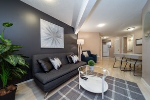 Relax in this stylish living room with a sofa, coffee table, and abstract art, leading to a dining area and kitchen.