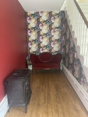 Habitación de esquina con pared roja, papel tapiz floral, sofá rojo y estufa antigua.