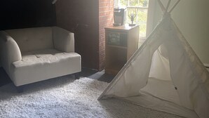 Een gezellige kamer met een witte bank, een wit tapijt en een tentachtige constructie.