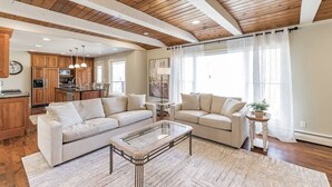 A spacious living room with a wooden ceiling, a large sofa, a glass coffee table, and a kitchen in the background. - Heavenly Home/Minnetonka Lakes/Nature Scenic View (Minnetonka)