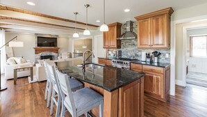 A spacious kitchen with wooden cabinets, a central island with bar stools, a fireplace, and a dining area with a sofa and chairs. - Heavenly Home/Minnetonka Lakes/Nature Scenic View (Minnetonka)