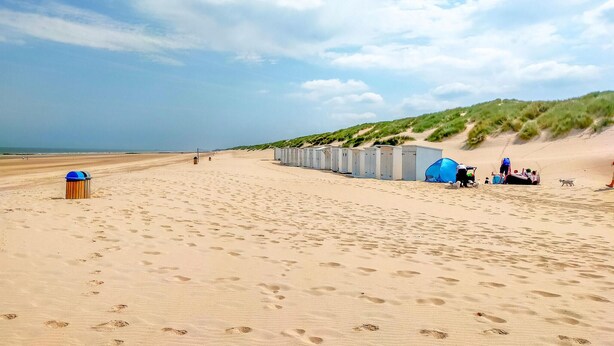 Une plage équipée de toilettes portables, d’une poubelle et d’une tente installée sur le sable.