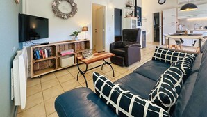 Un salon avec un canapé, un téléviseur, une bibliothèque, une cheminée et, au fond, un coin cuisine.