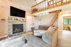 Ein gemütliches Wohnzimmer mit Kamin, großem Flachbildfernseher, einer Holztreppe und einer bequemen Sitzecke.