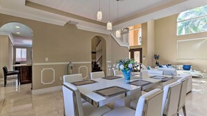 Un'ampia sala da pranzo con un tavolo grande e sedie, una scala e un angolo salotto con un divano e piante decorative.