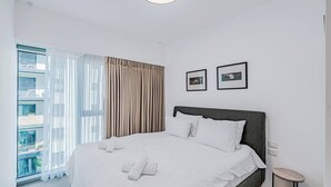 Moderni hotellihuone, jossa on suuri sänky, pieni sivupöytä ja parveke, jolta on näkymä.