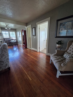 A spacious living area with hardwood flooring, a sofa, a dining table with chairs, and a kitchen in the background. - Clean and cozy 3 bdrm one bath home in the heart of Rupert.  (Rupert)