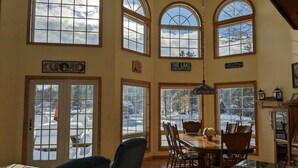 A dining area with a wooden table and chairs, large windows with snow outside, and a sign that says "The Lake is my happy place." - Beautiful Waterfront Home in Colton Near Local Colleges (Colton)