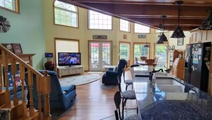 A spacious living room with a large TV, a dining area, and a kitchen with a central island. - Beautiful Waterfront Home in Colton Near Local Colleges (Colton)