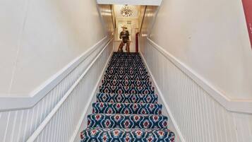 A staircase with patterned carpet and white railings leading to a room with a chandelier.