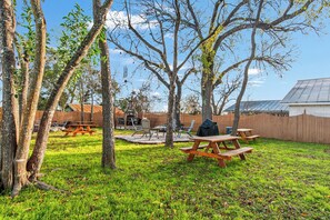 An outdoor patio area with picnic tables and a barbecue grill, surrounded by trees and a wooden fence. - Carriage Utopia 4 | Pet-Friendly Stay in Bandera (Bandera)