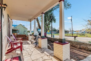 A covered outdoor area with stone flooring, wooden benches, and a view of a road and buildings in the distance. - Carriage Utopia 4 | Pet-Friendly Stay in Bandera (Bandera)
