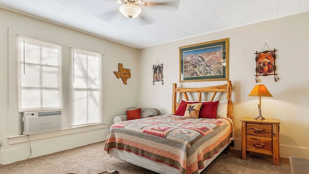 A bedroom with a large bed, a wooden headboard, a nightstand with a lamp, a wall painting, and a decorative wall hanging. - Carriage Utopia 4 | Pet-Friendly Stay in Bandera (Bandera)