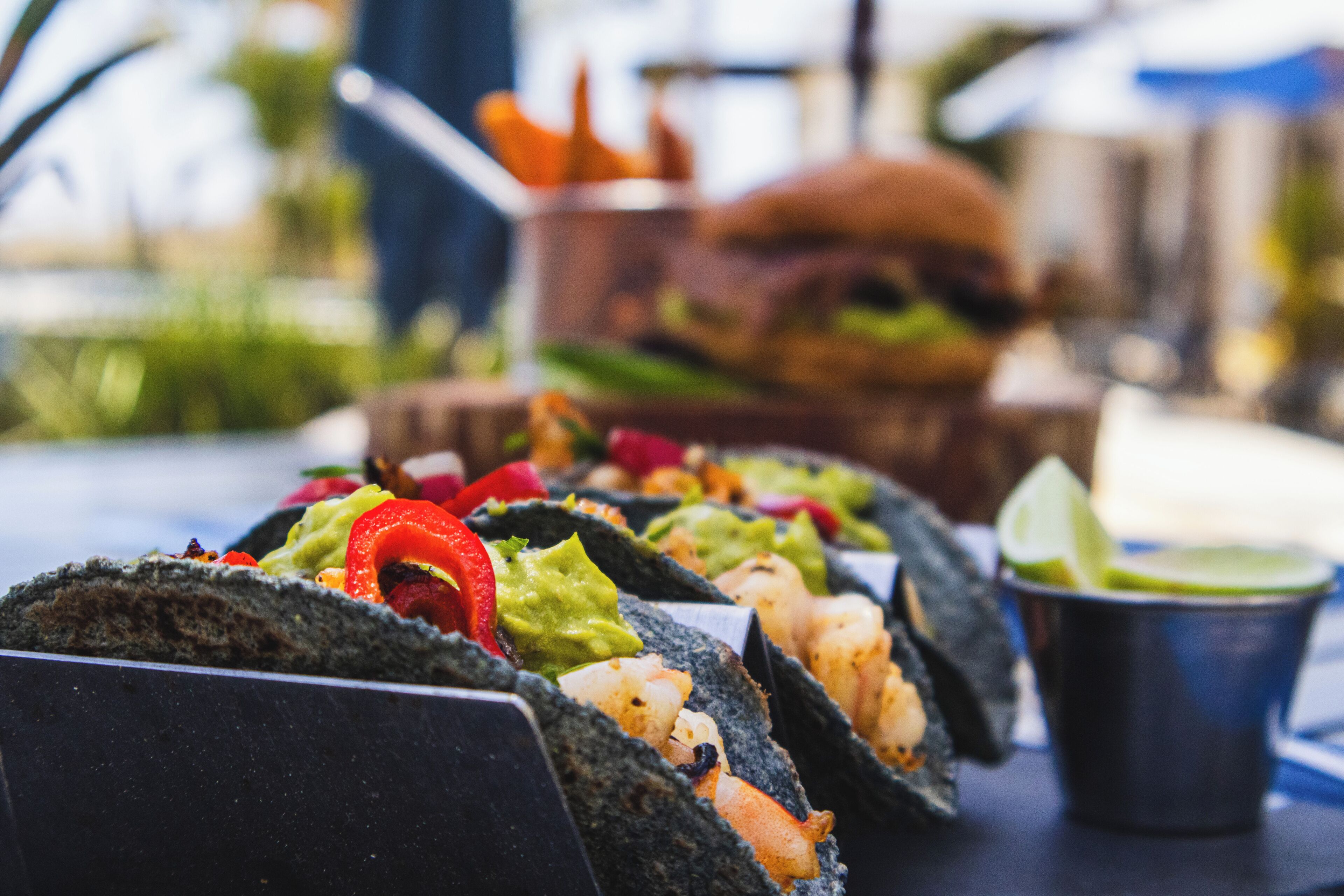 Una mesa con tres tacos, una hamburguesa y una taza de salsa.