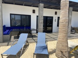 Un espacio al aire libre moderno con bancos acolchados azules y sillones de metal, un pilar de hormigón y una palmera.