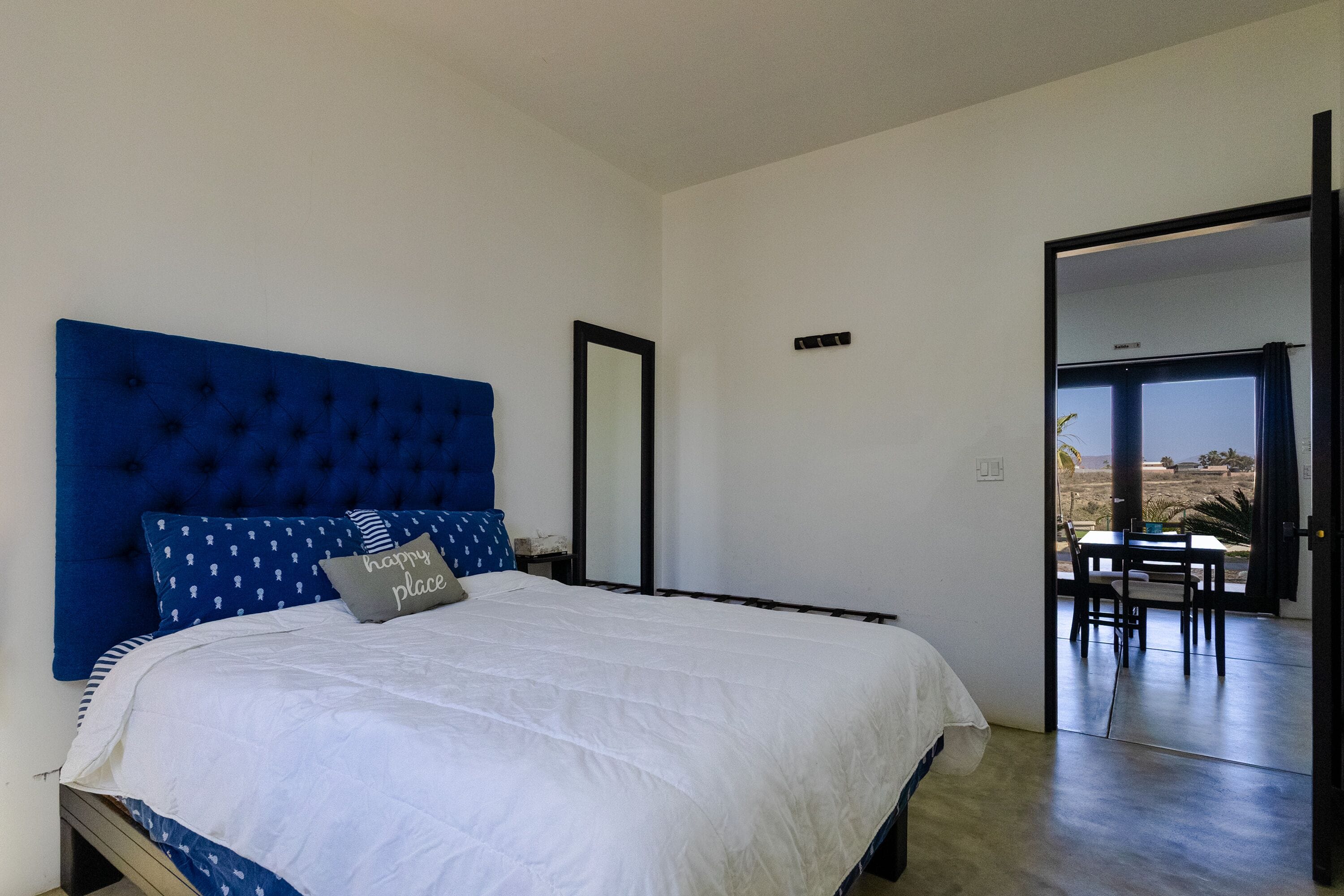 A bedroom with a large bed, a blue headboard, and a view through an open door to an outdoor area.