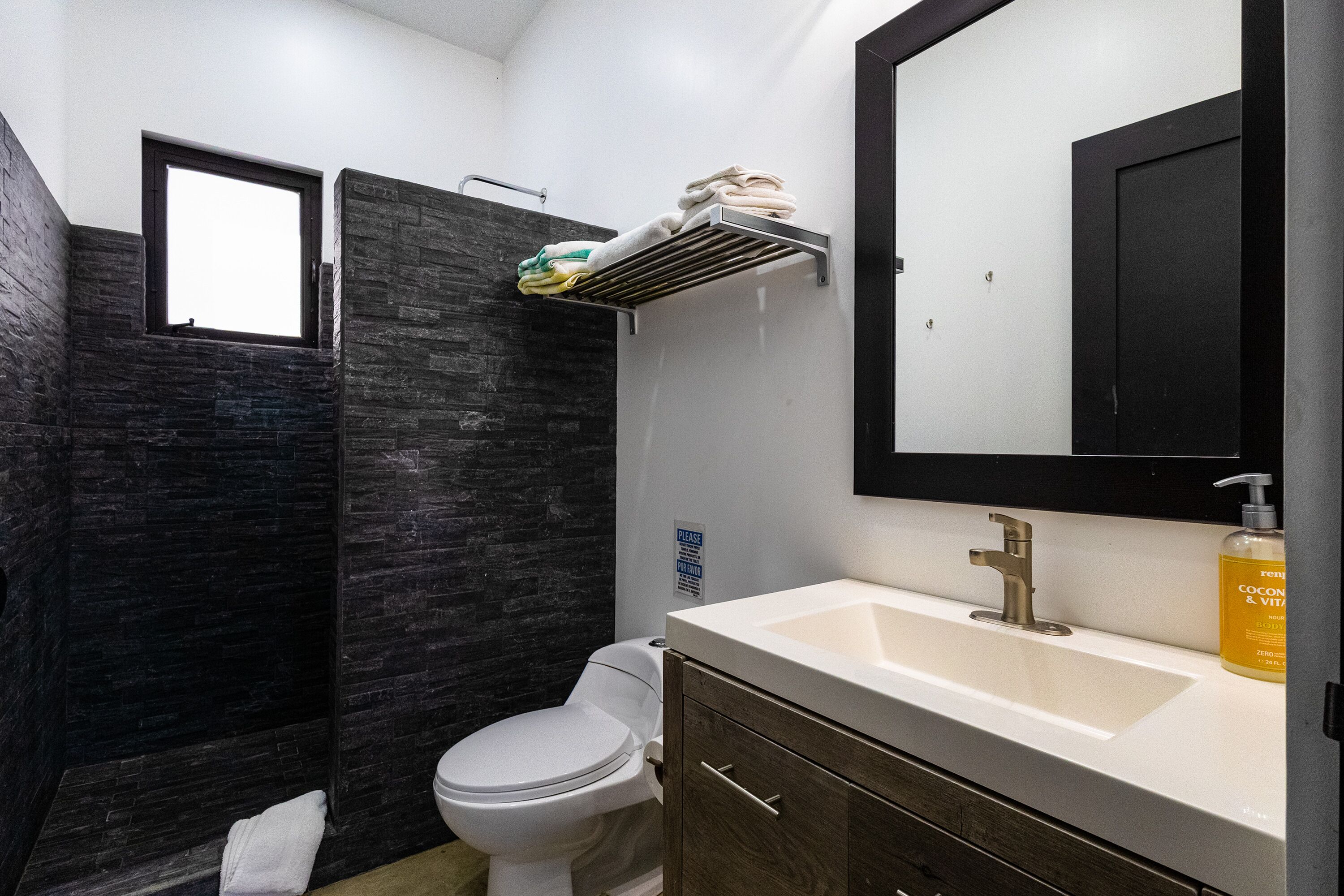 A bathroom with a white toilet, a sink with a mirror, and a shower area with dark tiles.