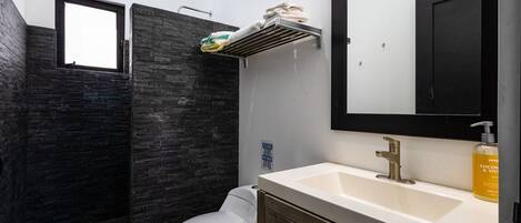 A bathroom with a white toilet, a sink with a mirror, and a shower area with dark tiles.