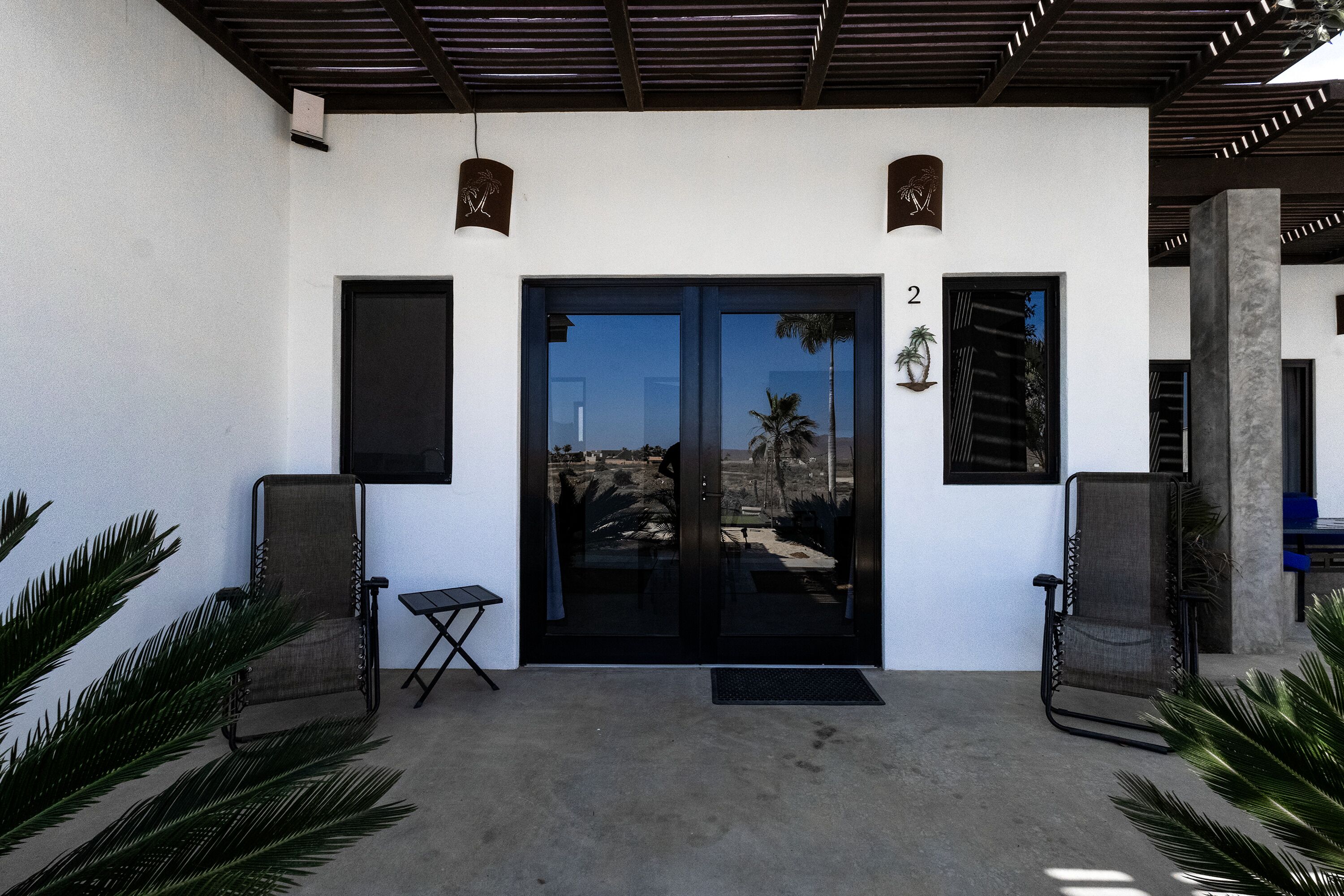 A building with a black-framed door, a small table, two chairs, and a number '2' on the wall.