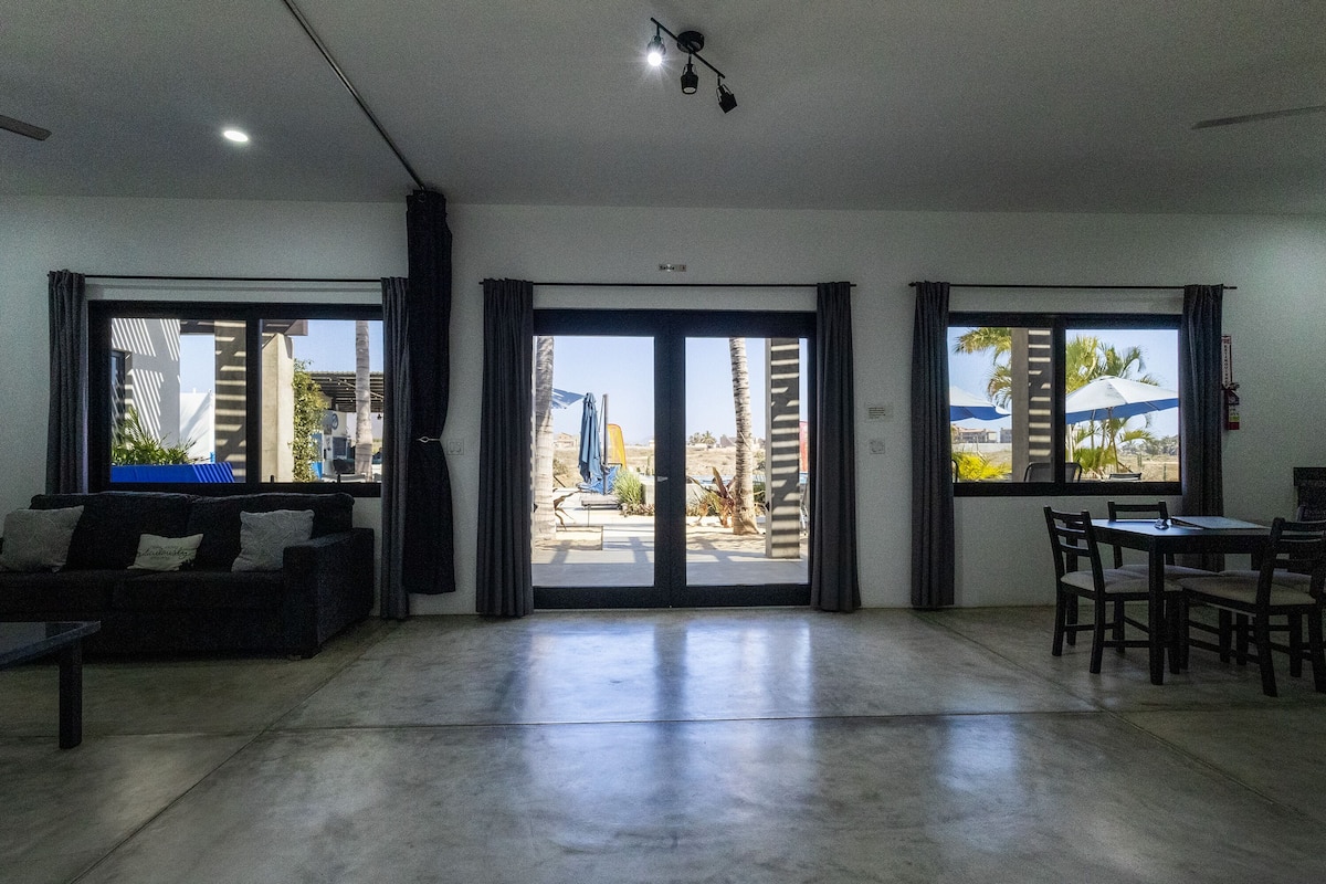 Amplia sala de estar con sofá, una mesa de comedor con sillas y grandes puertas corredizas de vidrio que dan a un patio exterior.