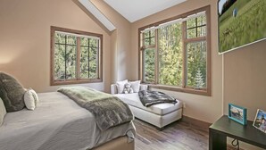 Un dormitorio con cama, sofá, ventanas amplias y televisor en la pared.