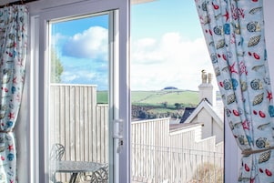 Una habitación con vistas a un paisaje rural, una puerta blanca y una mesa de metal con sillas.