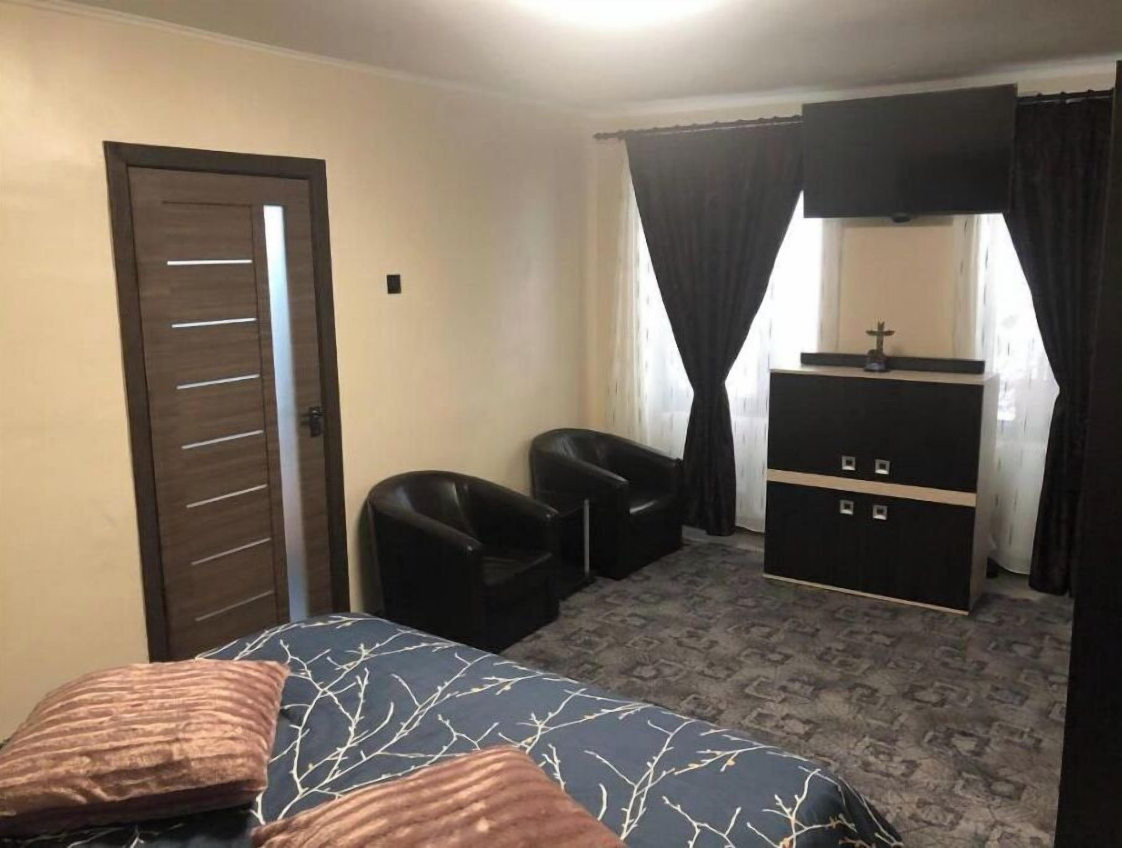 A hotel room with a bed, two chairs, a dresser, and a door.