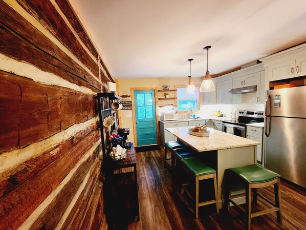 Une cuisine aux murs en bois, avec un îlot central doté de tabourets, des appareils en acier inoxydable et une porte bleue en arrière-plan.
