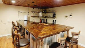 Et rustikt køkken med en træø-bar, barstole og et højt loft med synlige bjælker.
