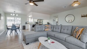 Ein modernes Wohnzimmer mit einem grauen Ecksofa, einem weißen Couchtisch und einem Essbereich mit einem Holztisch und Stühlen.