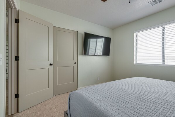 A bedroom with a bed, a TV mounted on the wall, and a window with blinds.