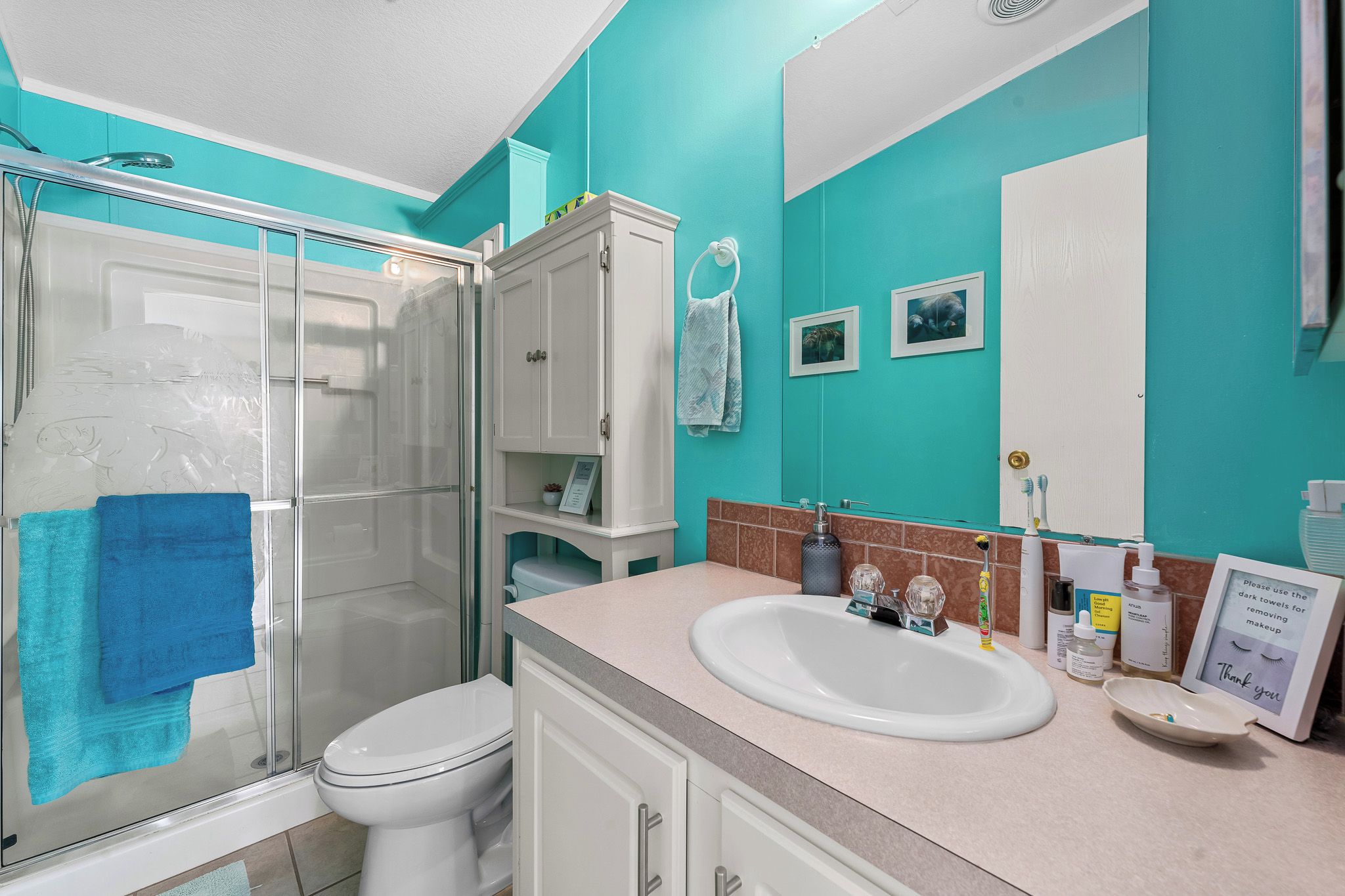 A bathroom with a glass shower enclosure, a white toilet, a sink with toiletries, and a mirror.