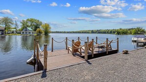 A wooden dock with chairs and a rope barrier, a boat docked on the water, and a house in the background. - Rustic Riverside Charm and Exclusive Fishing Access! (Richland)