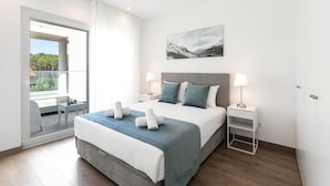 Une chambre moderne avec un grand lit, deux tables de chevet, une vue à travers une porte-fenêtre coulissante et un tableau représentant un paysage de montagne accroché au mur.