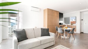 Un salon moderne comprenant un canapé, une table à manger avec des chaises, un coin cuisine et une grande fenêtre.