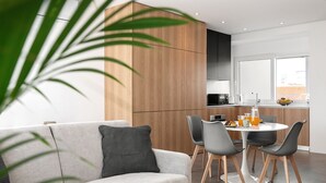 Une cuisine moderne avec un coin repas, comprenant un canapé gris, des chaises noires et une table ronde agrémentée d’un panier de fruits.